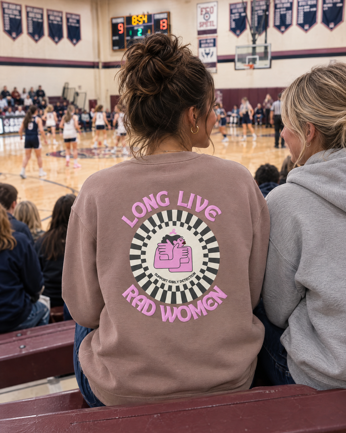 A woman at a basketball game wearing the Long Live Rad Women sweatshirt, back print showing.