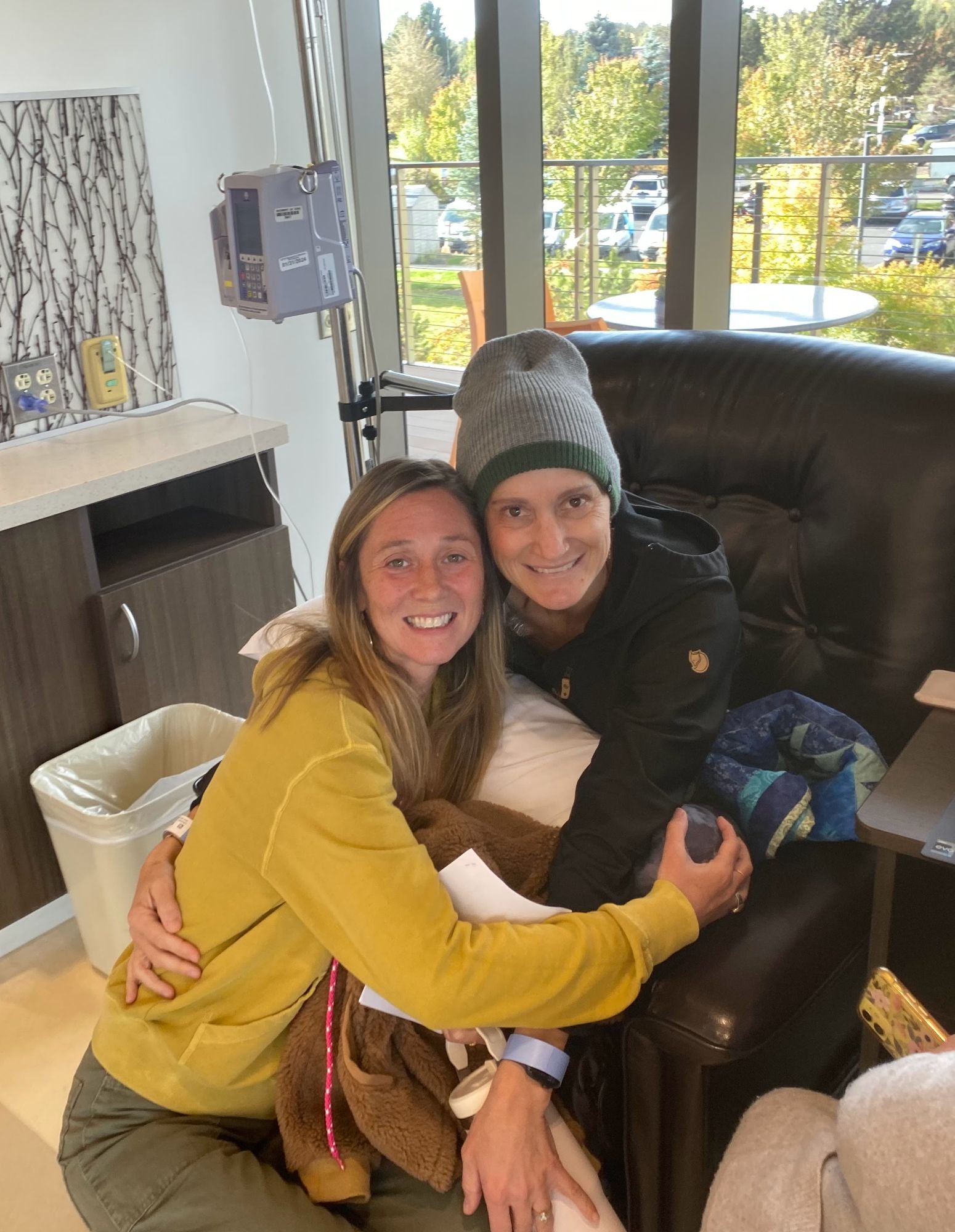 Two friends hug and smile in a treatment room.
